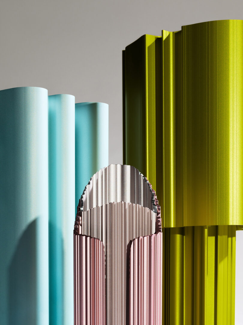 An array of upright cylindrical objects in shades of blue, green, and pink, each with ridged surfaces, artistically arranged against a grey background.