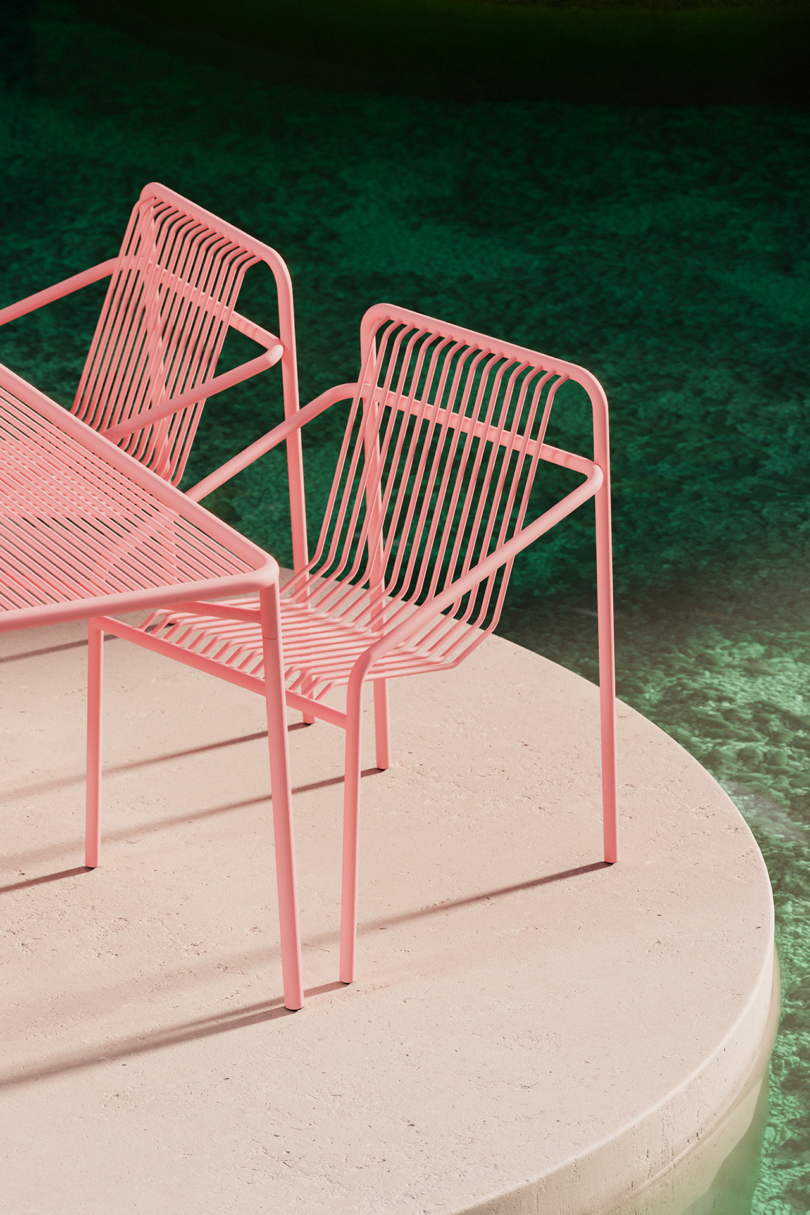 Modern pink outdoor furniture set on a circular concrete platform surrounded by water.