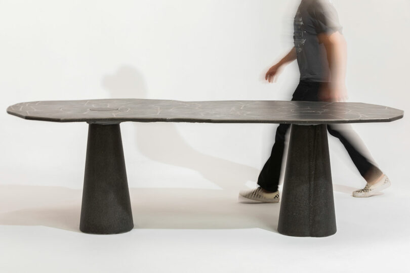 A person walks past a modern table with a concrete top and cylindrical bases.