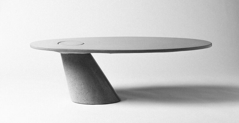 A minimalist James De Wulf concrete table with a circular top and a tapered cylindrical base.