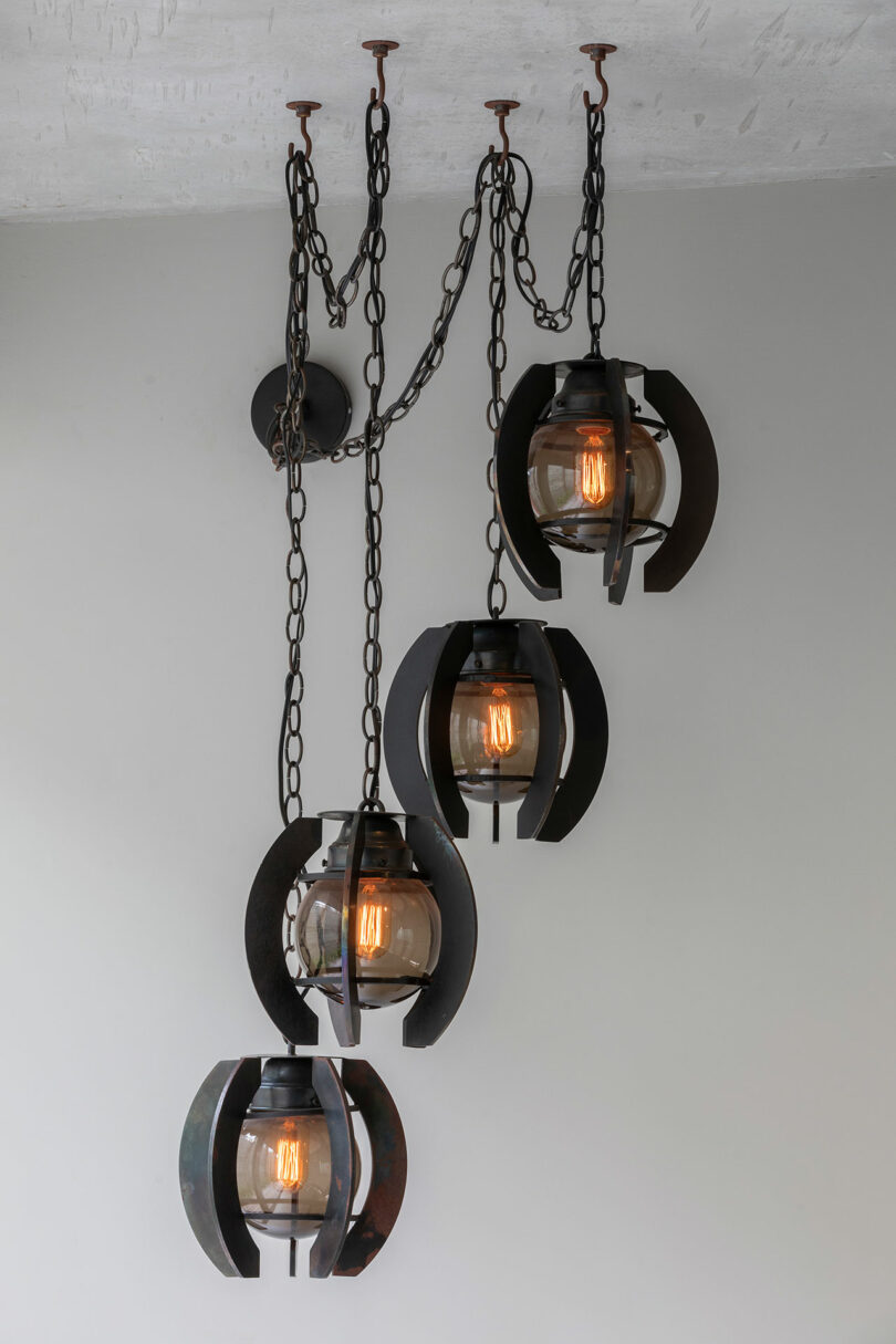 A James De Wulf modern chandelier with four industrial-style pendant lights suspended by chains from the ceiling.