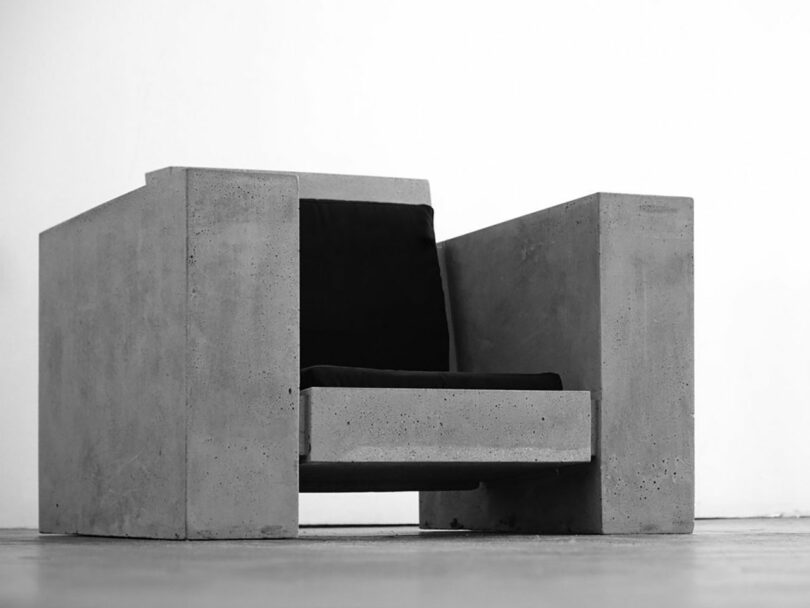 Modern concrete armchair with black cushions on a plain background.