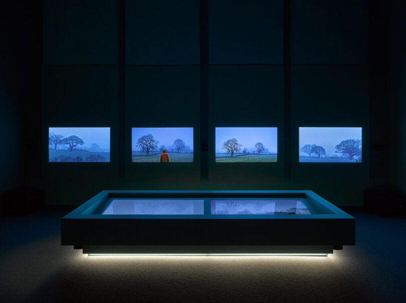 Artist Sir John Akomfrah's  ‘Listening All Night To The Rain,’ video display installation with four OLED display on the wall and one large floor mounted display underlit with LED lights in a darkened room.