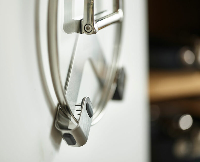 نمای نزدیک از درب‌های فلزی قابلمه آویزان روی قفسه آشپزخانه، با تمرکز روی دسته درب جلو.