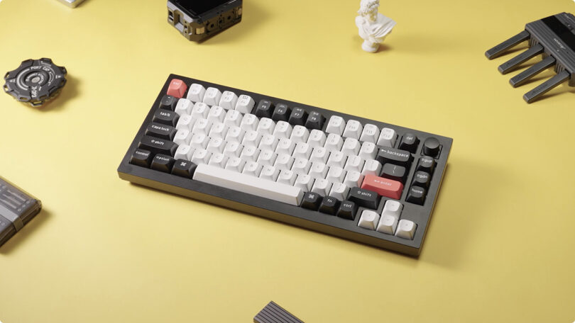 Keychron Q1 HE mechanical keyboard with custom keycaps on a yellow surface surrounded by disassembled computer parts.