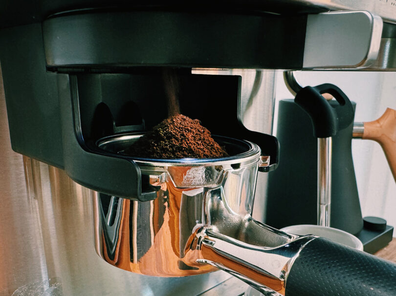 A close-up of a KitchenAid Espresso Collection machine dispensing freshly ground coffee into a portafilter.