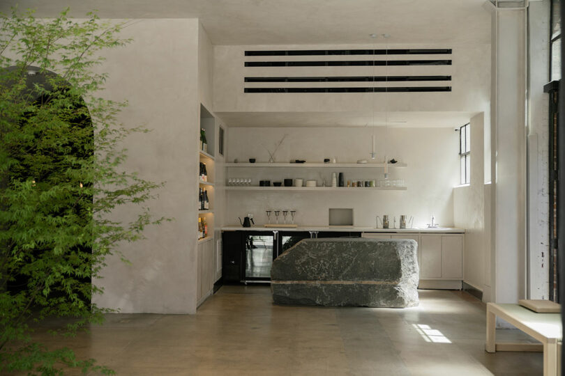 Modern kitchen with minimalist design featuring a large natural stone island and concrete floors.