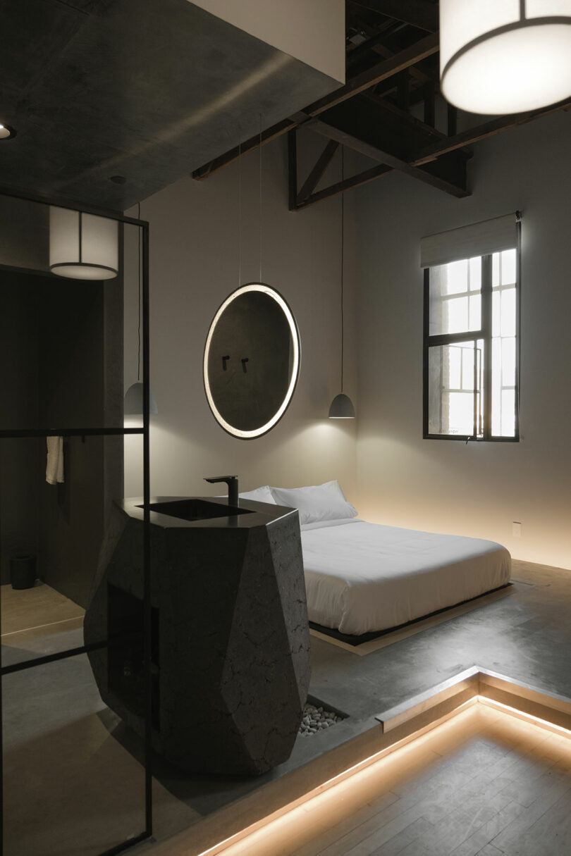 Modern minimalist bedroom with an industrial aesthetic, featuring a concrete platform bed, sleek fixtures, and warm lighting accents.