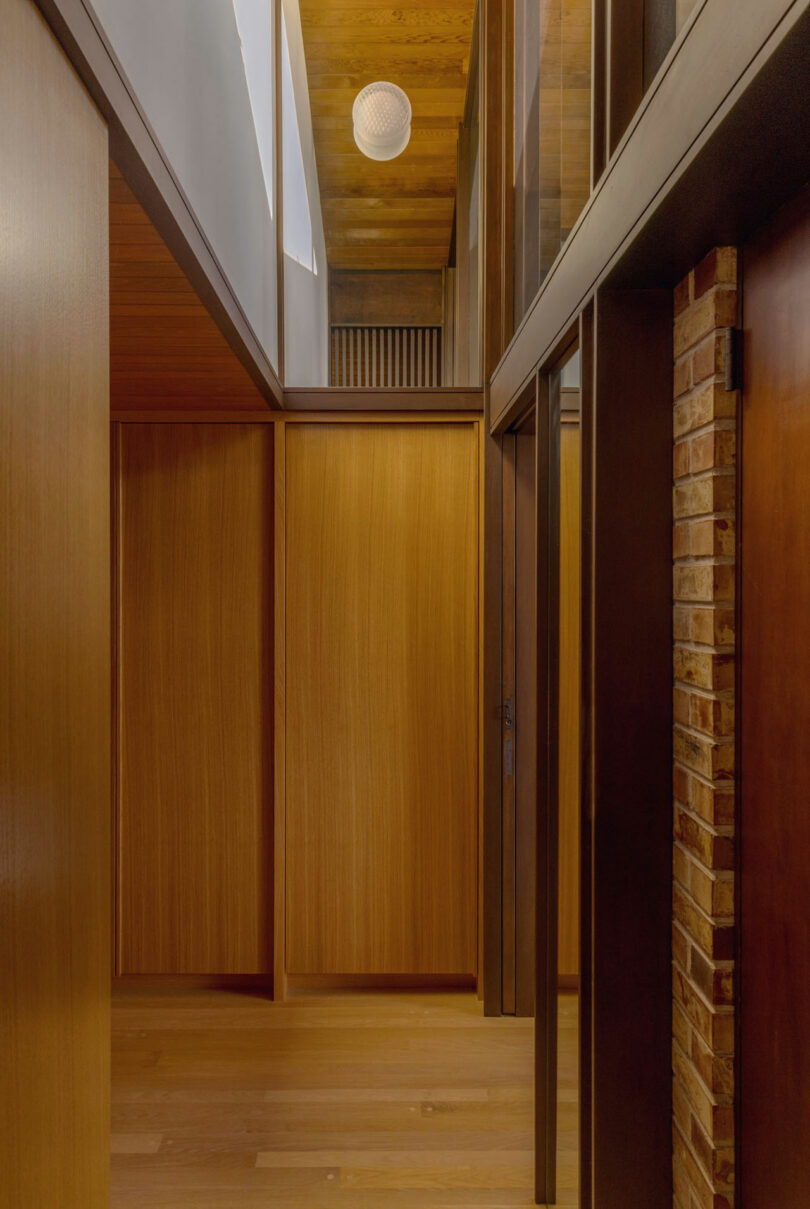Narrow hallway in a modern home featuring wooden paneling and walls, with a high ceiling and a round ceiling light.