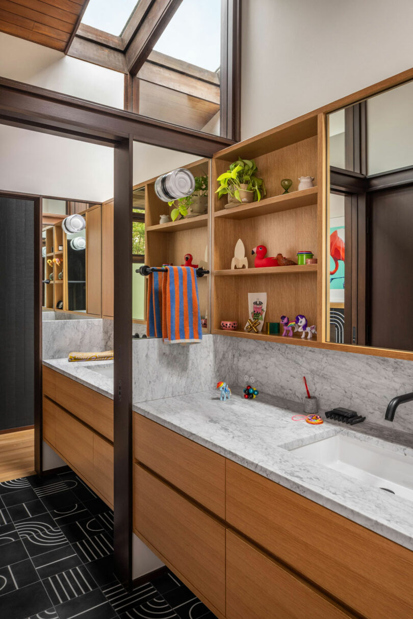 Modern bathroom with a marble countertop, integrated sink, built-in wooden shelving filled with decorations, and geometric-patterned floor tiles.