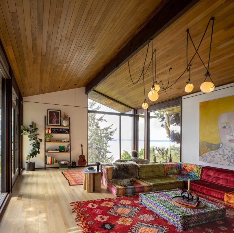 Modern living room with colorful furniture, wooden ceiling, and large windows overlooking a lake.