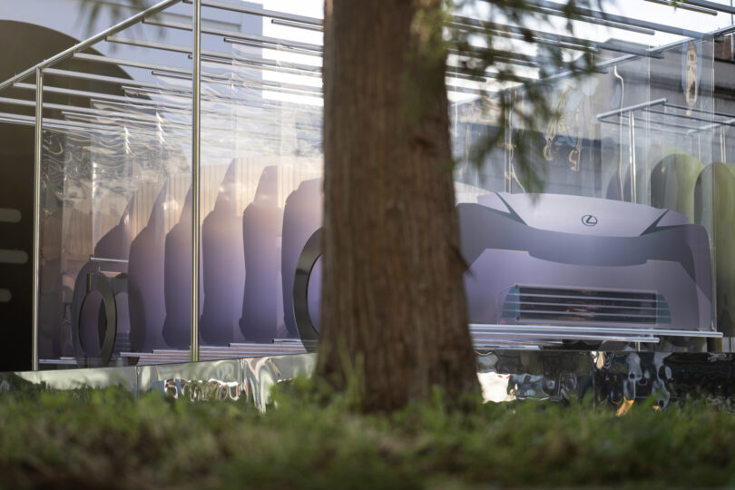 Marjan van Aubel's "8 Minutes and 20 Seconds" depicting the Lexus Future Zero-Emission Catalyst concept car made from sheets of solar cells affixed to transparent, colorful acrylic sheets, shot from ground level from behind a real tree trunk.