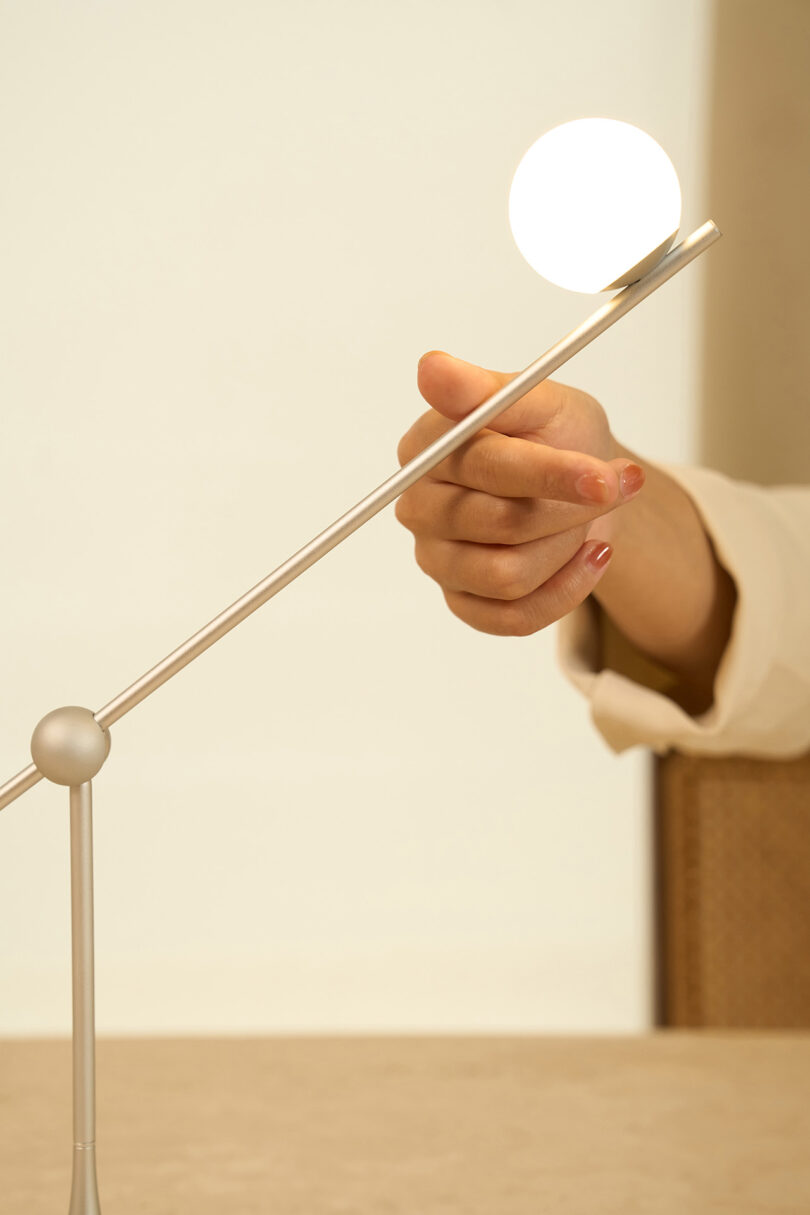 A person's hand adjusting the angle of a modern Lumio Ovo table lamp with a spherical white light.