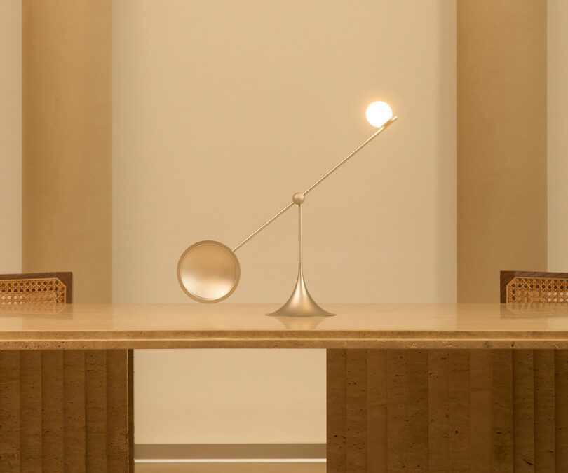 Modern Lumio Ovo table lamp with an illuminated spherical bulb and a circular domed shade, poised on a table in a room with soft lighting and tan walls with its right side angled upward.