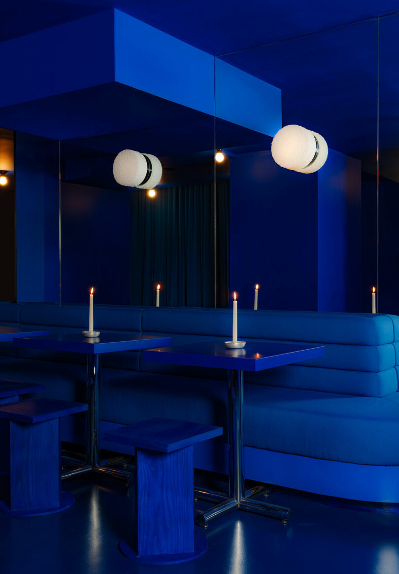 Modern blue-toned lounge with candlelit tables, spherical pendant lights, and plush seating under a geometric ceiling.