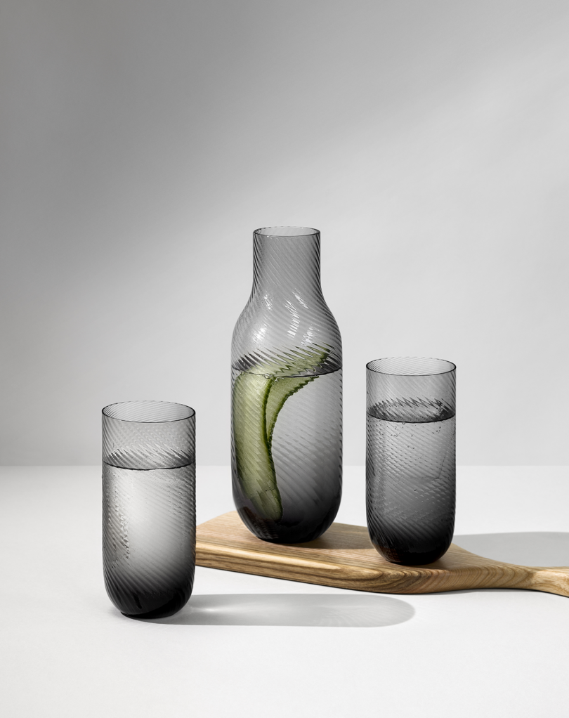 Glassware carafe and two glasses.vase, all placed on a surface with a wooden spoon beside them.