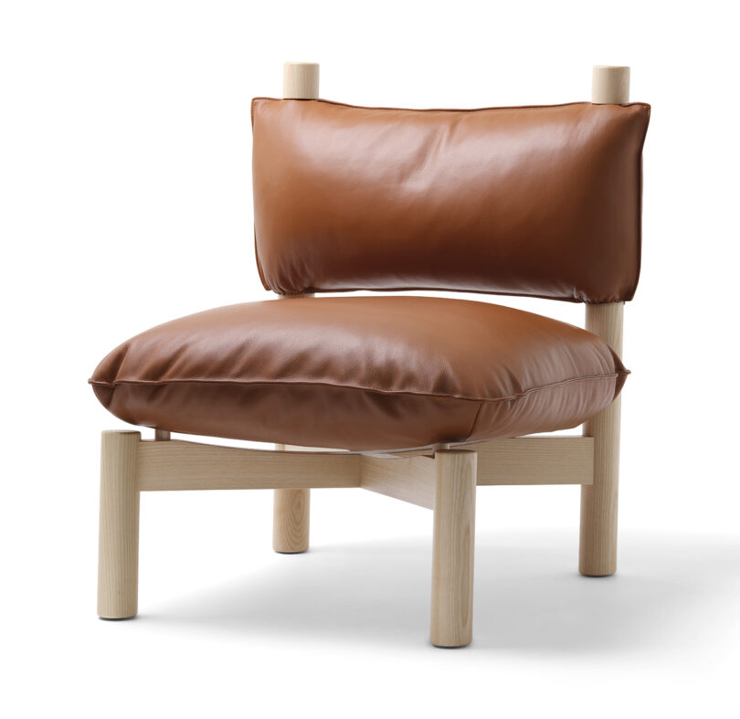 A modern chair featuring a light wooden frame and oversized, cushioned leather pads in brown, isolated on a white background.