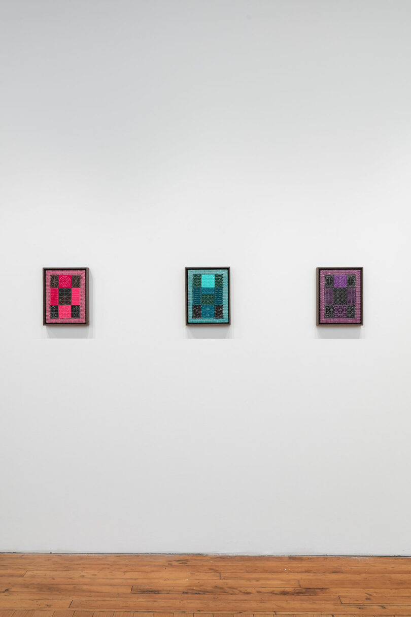Three framed digital artworks featuring geometric patterns in pink, blue, and purple hues, displayed on a white gallery wall.