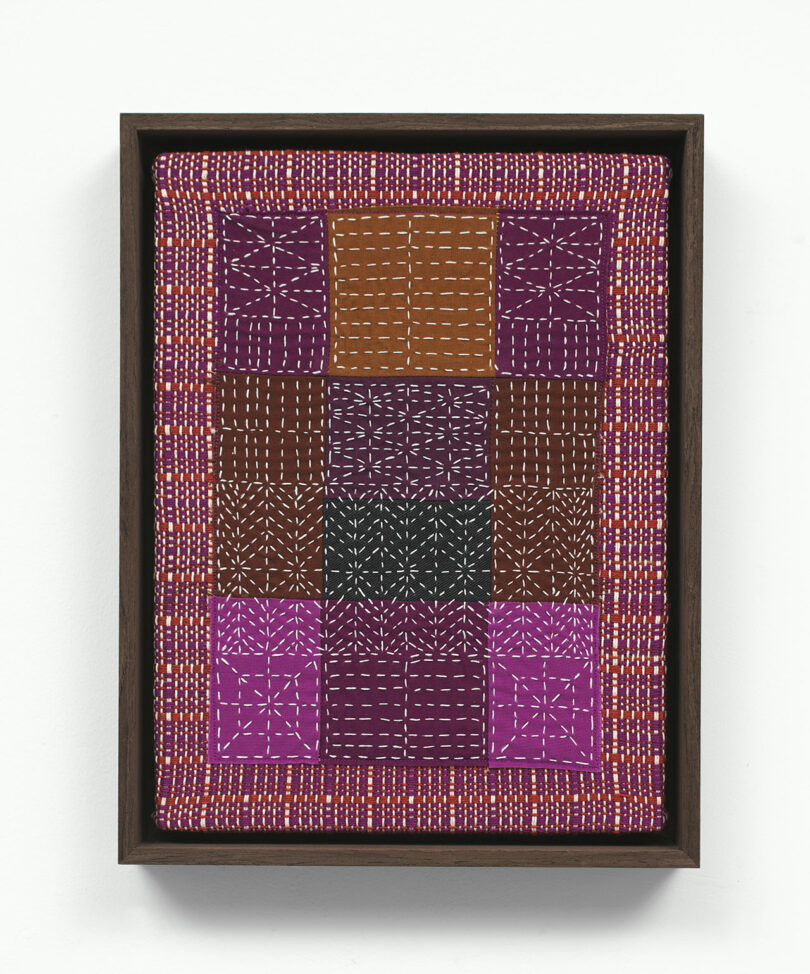 Aboriginal dot painting with geometric patterns in a wooden frame, featuring a symmetrical arrangement of earthy and white dots on a dark background.