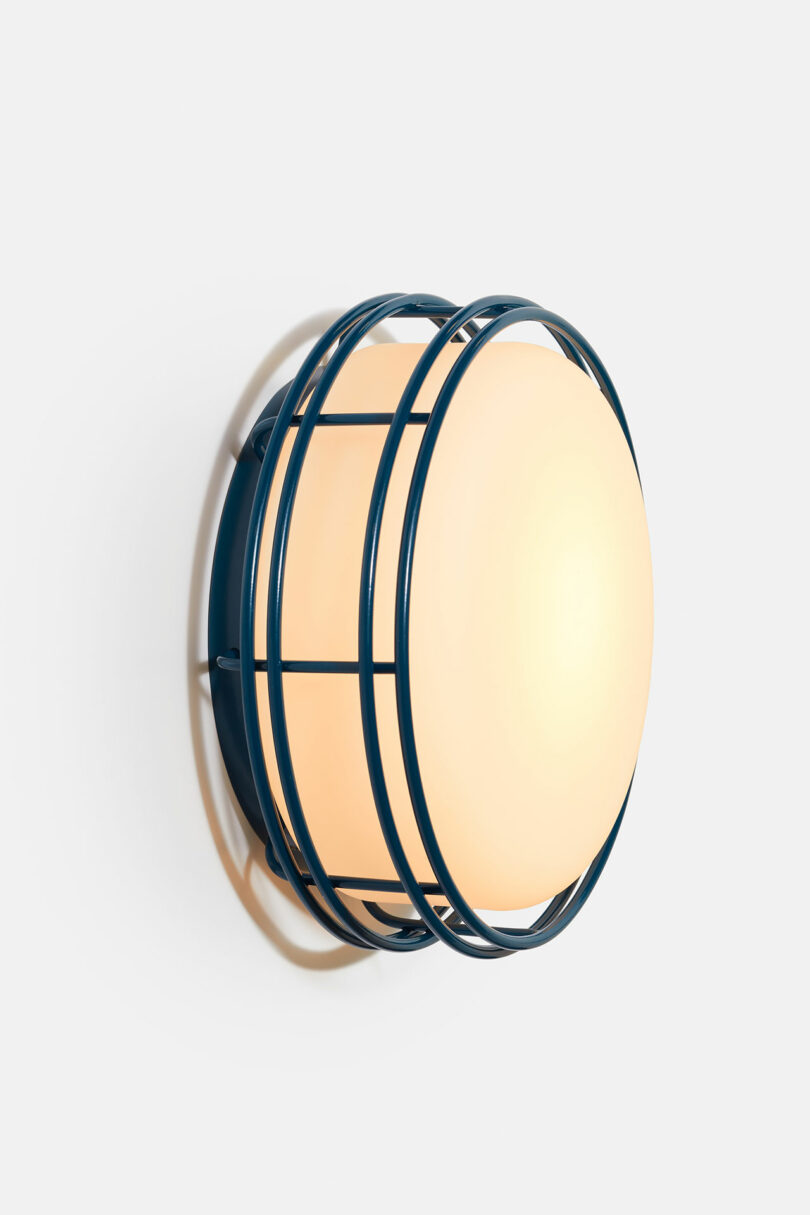 A round wall-mounted lamp with a frosted glass front and a dark blue metal cage design against a white background.