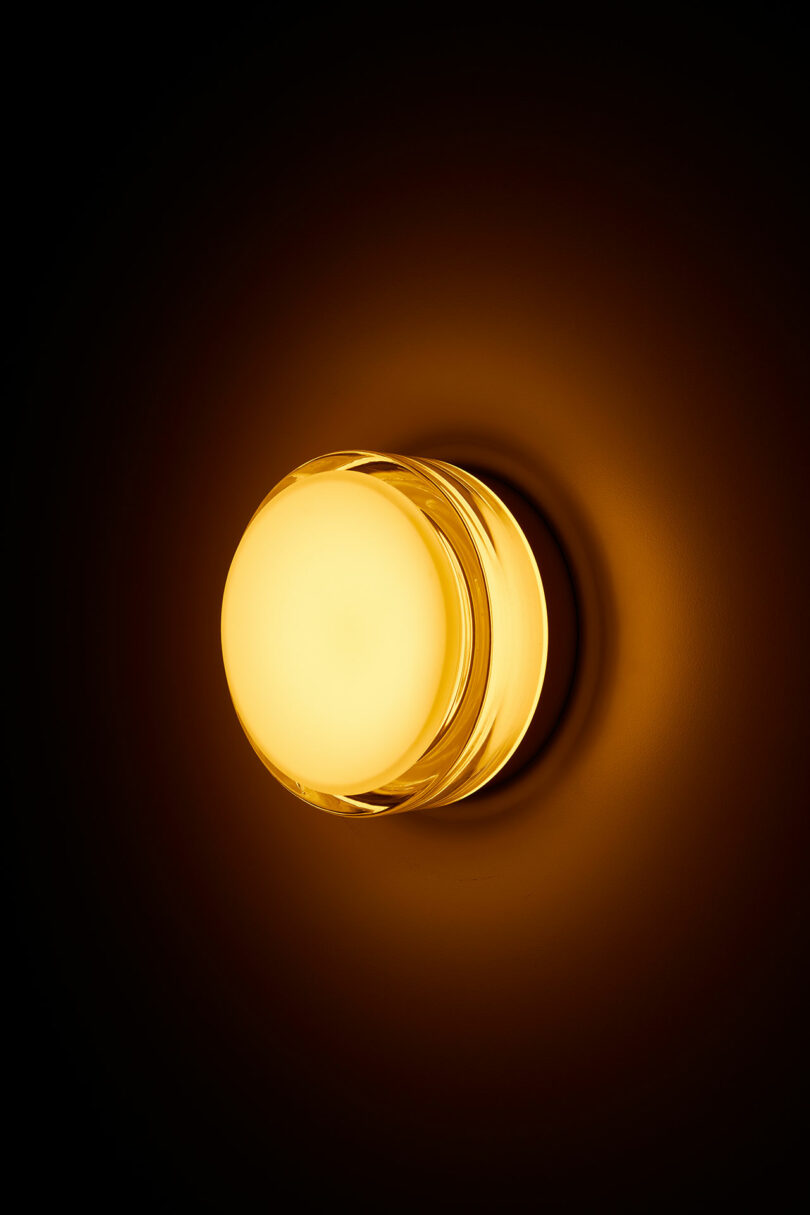 A glowing round wall light emitting a warm yellow light against a dark background.
