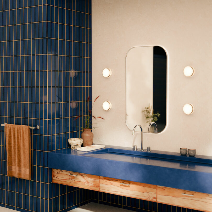 Modern bathroom featuring a blue vanity with a wooden front, a rectangular mirror flanked by round lights, and cobalt blue tile walls.