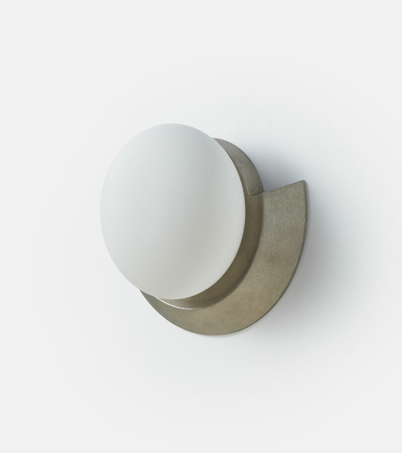 A round white light fixture attached to a curved metallic base against a plain white background.