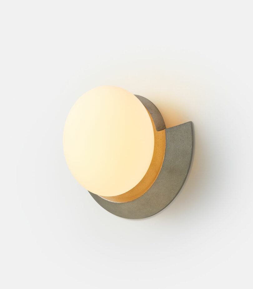 A modern wall-mounted light fixture with a half-circle design and a warm, illuminated globe against a plain white background.