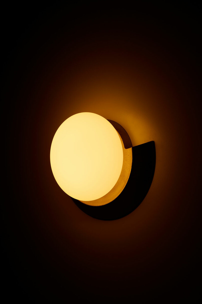 A round, wall-mounted light emitting a warm, soft glow in a dark room, creating a halo effect on the surrounding surface.