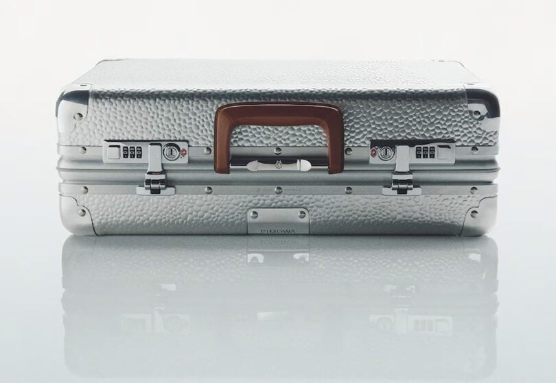 Silver Rimowa hardshell aluminum hammer textured suitcase with brown handle and combination locks.