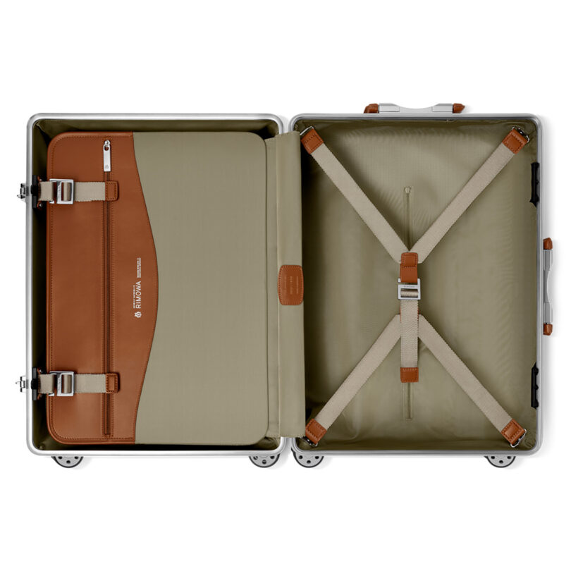 Open empty Rimowa luggage with tan leather and green nylon interior and securing cross straps.