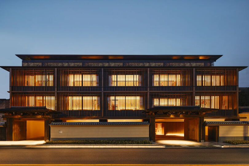 Modern three-story Six Senses Kyoto hotel at dusk, featuring illuminated horizontal wooden slats and multiple warm-lit windows, with lobby entry at ground floor.