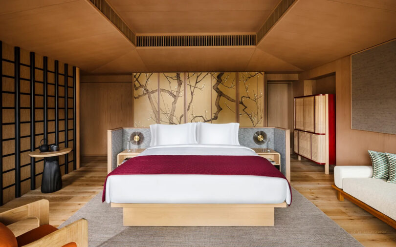 Modern Japanese-style bedroom at the Six Senses Kyoto hotel featuring a neutral color scheme, a large bed with a red coverlet, wooden paneling, and traditional decorative elements like shoji screens.