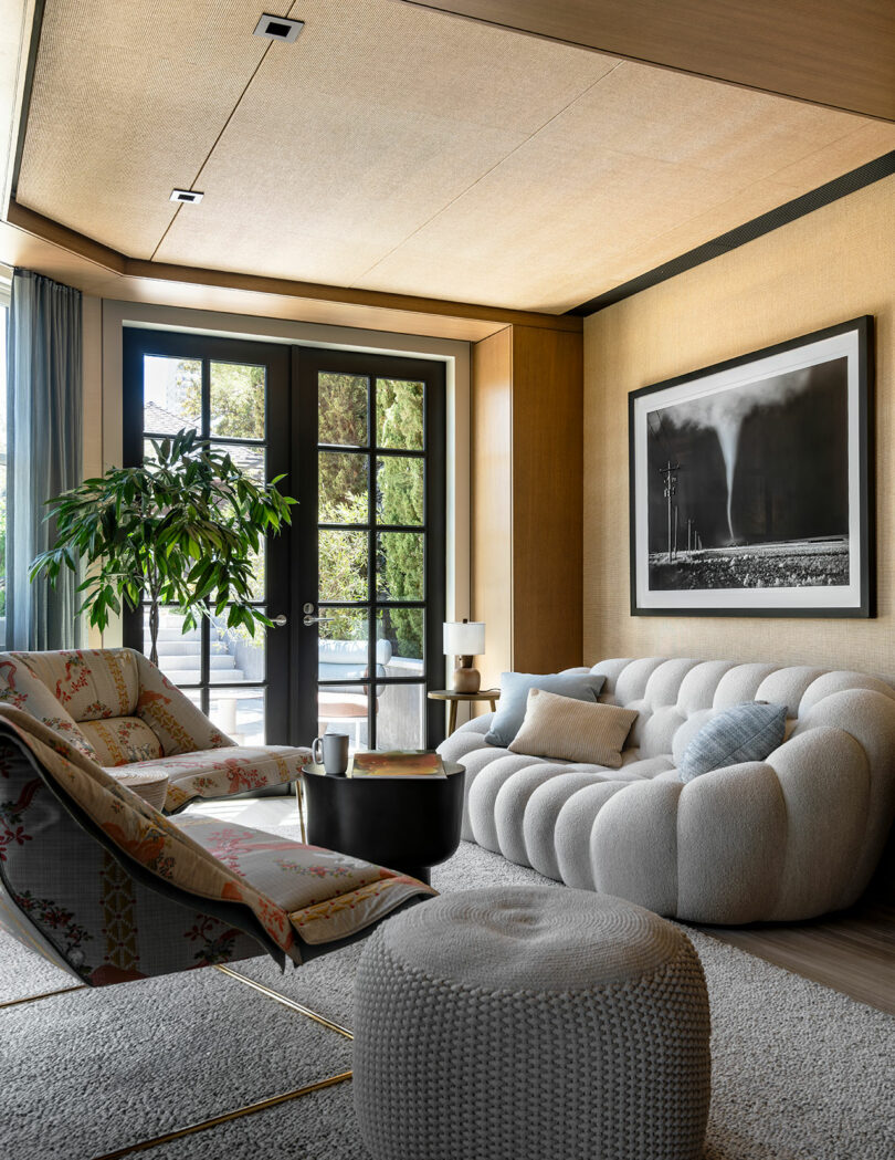 Modern living room designed by SkB Architects, featuring a plush white sofa, patterned armchair, and large windows overlooking trees with wooden walls and a ceiling.