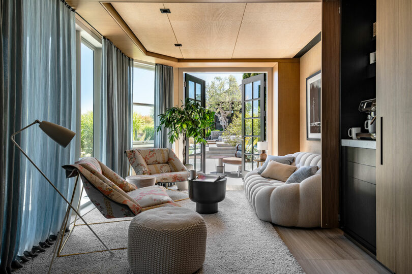 Modern living room designed by SkB Architects, with stylish furniture, floor-to-ceiling windows, and a plant, seamlessly connecting to an outdoor patio.