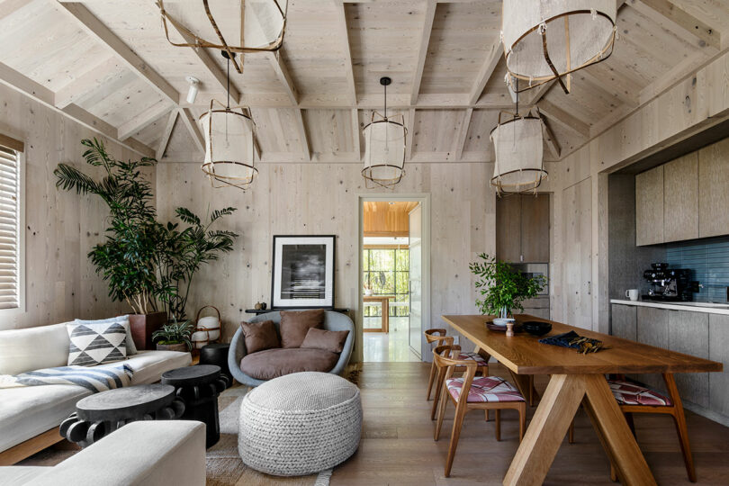 Modern rustic living room designed by SkB Architects, featuring exposed wooden beams, stylish furniture, circle chandeliers, and a plant beside a large window.