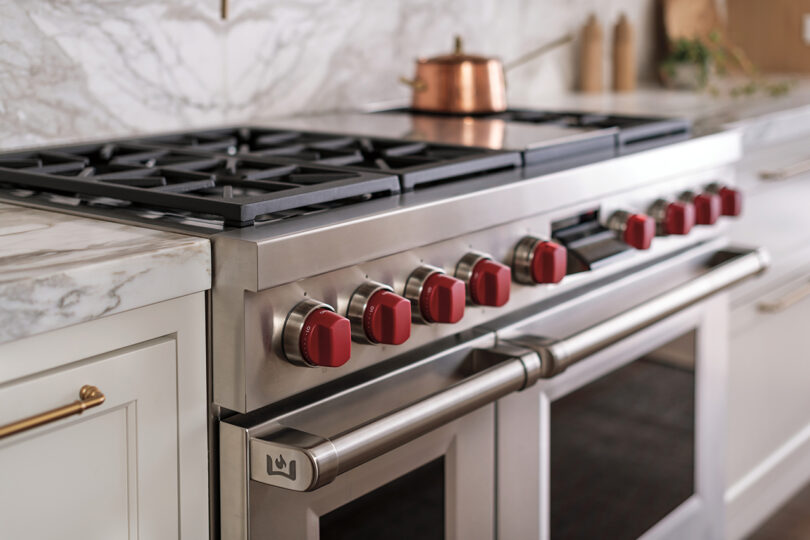 Luxurious modern kitchen featuring a stainless steel gas stove with red knobs and a white marble countertop.