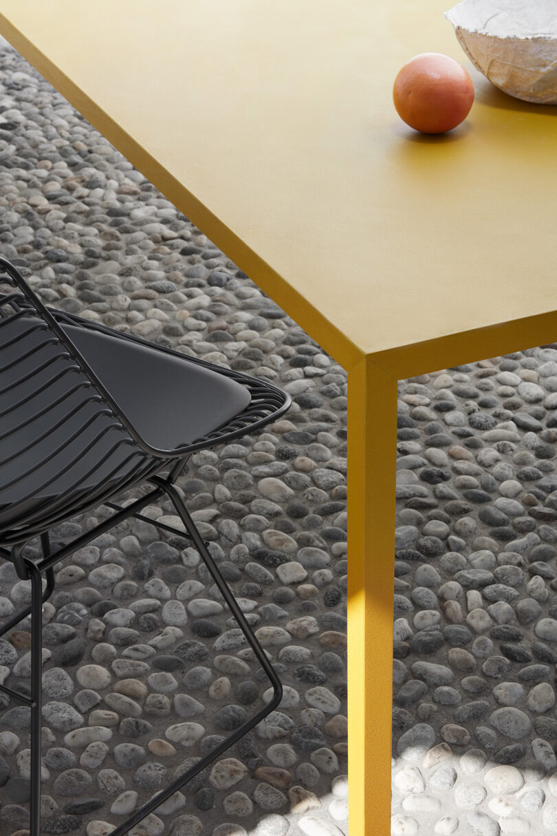 Corner of yellow outdoor table and black chair.