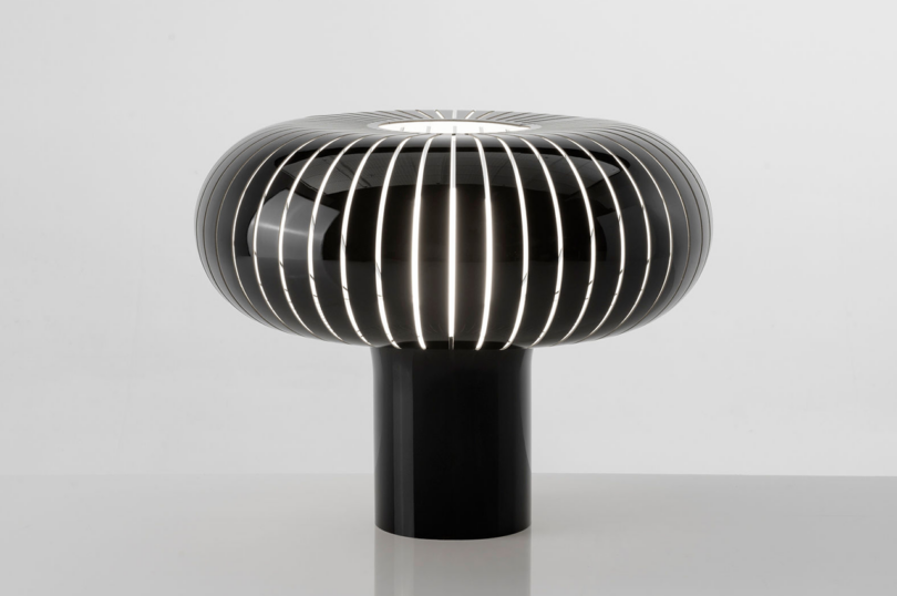 Modern metal slatted table lamp with a glowing center on a white background.