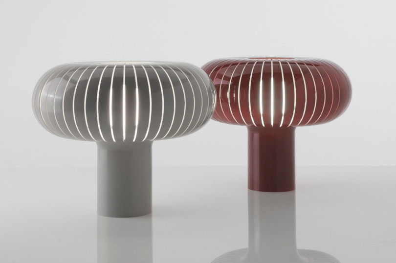 Two modern, ribbed table lamps with reflective surfaces, one silver and one red, on a white background.