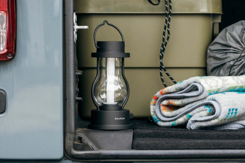 A portable black lantern resting beside a rolled-up blanket in the storage compartment of a vehicle.