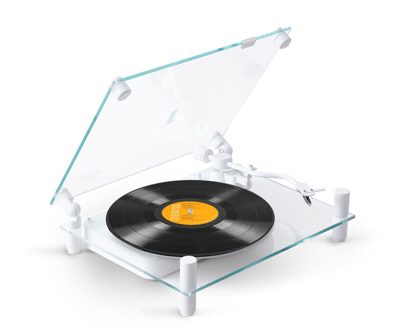Modern transparent turntable playing a vinyl record with yellow center label. Turntable glass cover is partially angled open.