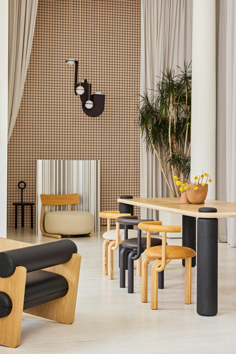 Modern interior with wooden tables, black and beige chairs, a tiled wall, hanging lamps, and indoor plants.