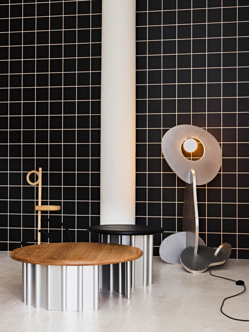 Modern interior with black tiled wall, wooden round table, abstract metal lamp, and a wooden chair with a minimalist design.