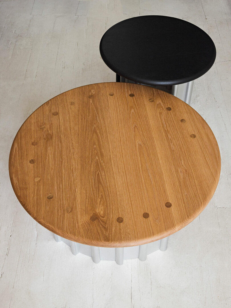 A wooden oval table with black stool on a concrete floor, showcasing natural wood grains and a smooth, contemporary design.
