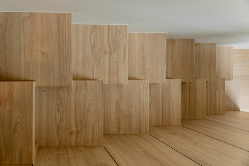 A series of tall wooden panels in varying heights arranged in a staggered line on a wooden floor in a room.