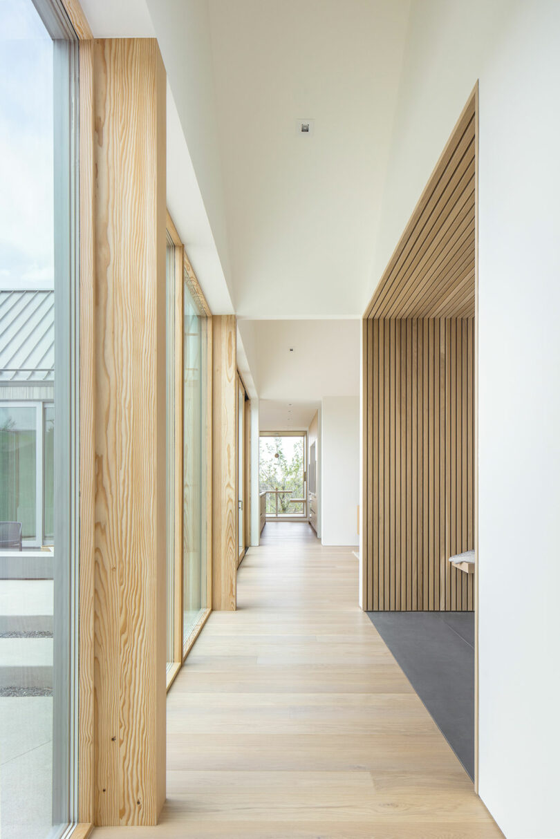 Modern hallway in Villa H featuring wooden floors and walls with large windows, allowing ample natural light into the space.