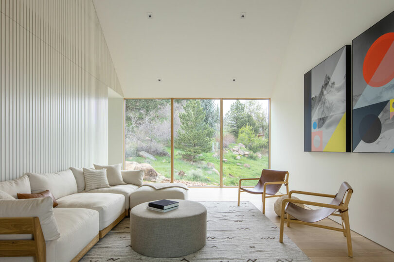Modern living room in Villa H with a large sectional sofa, a wooden chair, abstract art, and floor-to-ceiling windows showing a natural landscape.