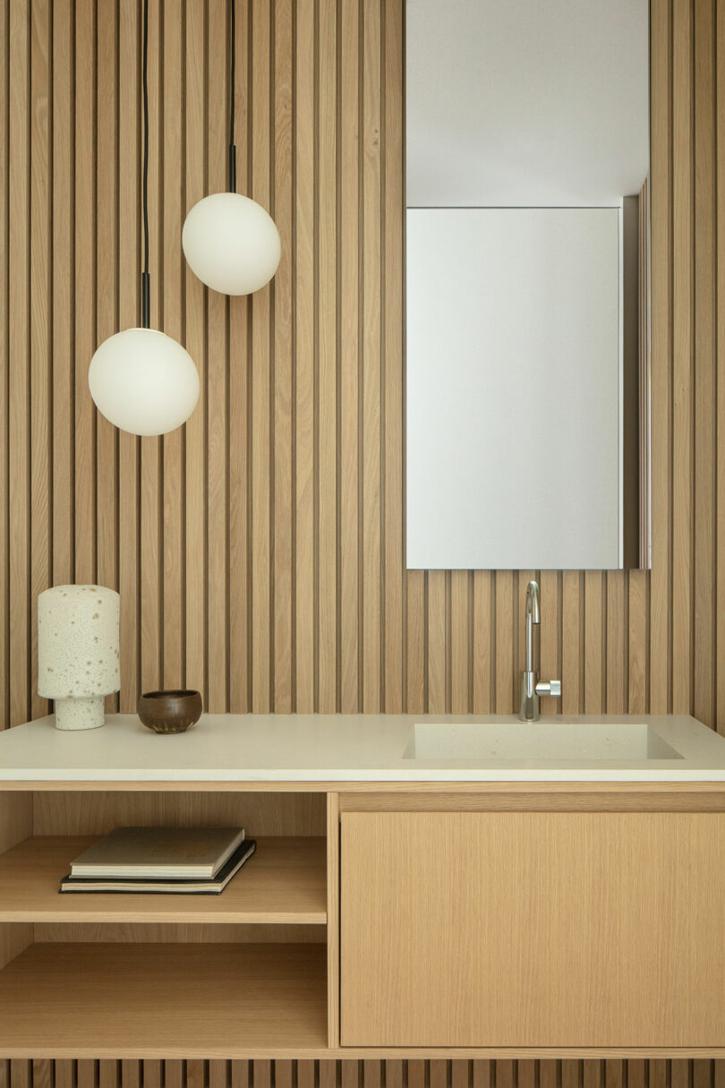 Modern minimalist Villa H bathroom with wooden slat walls, a white countertop sink, and hanging spherical pendant lights.