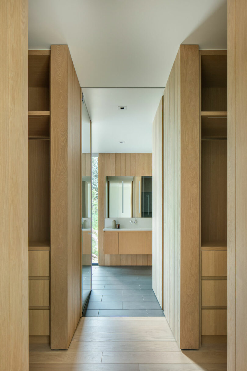 Modern hallway in Villa H with wooden cabinets lining the walls and a visible bathroom at the end, featuring a sink and mirror.